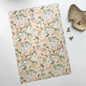 May include: A sheet of yellow wrapping paper with a repeating pattern of white flowers and lemons. The lemons are illustrated in a realistic style with a golden yellow color.
