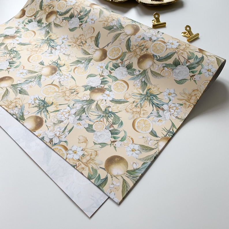 May include: A sheet of yellow wrapping paper with a floral pattern featuring white flowers and yellow lemons. The paper has a subtle texture and is perfect for wrapping gifts.