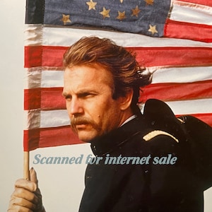 May include: A man in a dark blue uniform with a gold trim holds a large American flag. He has a mustache and is looking to the right. The flag is waving in the wind. The text "Scanned for internet sale" is visible in the lower right corner of the image.