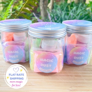 May include: Three clear plastic jars with silver screw-top lids, each containing colourful packets labelled Magic Dust. The circular labels feature a pastel gradient and the text Magic Dust, Just add water. Each jar holds small bottles and supplies.