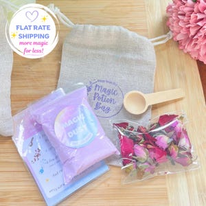 May include: A beige drawstring pouch labelled Magic Potion Bag, a clear plastic packet of purple Magic Dust, a small wooden scoop, a clear packet of dried pink rose buds, and an instructional card with text, all arranged on a wooden surface.