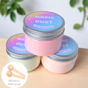 May include: Three clear plastic jars with silver screw-top lids containing colourful powder. Each lid features a circular label with a rainbow gradient background, white text reading Magic Dust, and the phrase Just add water. Two small wooden scoops.