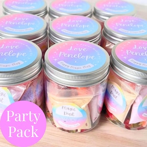May include: Several clear glass jars with silver lids, each adorned with a label reading "Love Penelope" and "Happy Magic Play." The jars contain colourful contents and small bags labelled "Magic Dust." A pink circle reads "Party Pack."