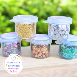 May include: Five clear plastic jars filled with various colours of chunky glitter. The jars have translucent lids with the text MAGIC GLITTER printed on them. The contents include gold, silver, multi-coloured, gold and pink, and blue and green flakes.