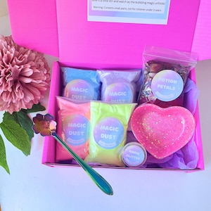 May include: A bright pink box containing four pouches of Magic Dust in blue, purple, pink, and yellow, a bag of Potion Petals, a small jar of Magic Glitter, and a heart-shaped pink dish with glitter, plus a flower-shaped iridescent spoon.