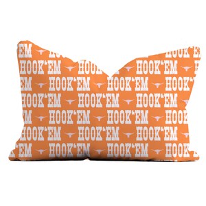 May include: Orange throw pillow with a white repeated pattern of the words "Hook 'Em" and a stylized Longhorn steer head.