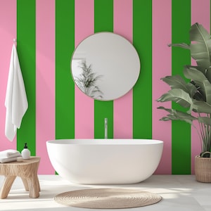 May include: A white bathtub sits in a bathroom with pink and green striped wallpaper. A round mirror hangs on the wall above the tub. A potted plant is on the right side of the image.