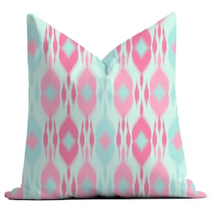 May include: A decorative throw pillow with a pink and blue geometric pattern. The pillow has a light blue background with pink and blue diamond shapes.