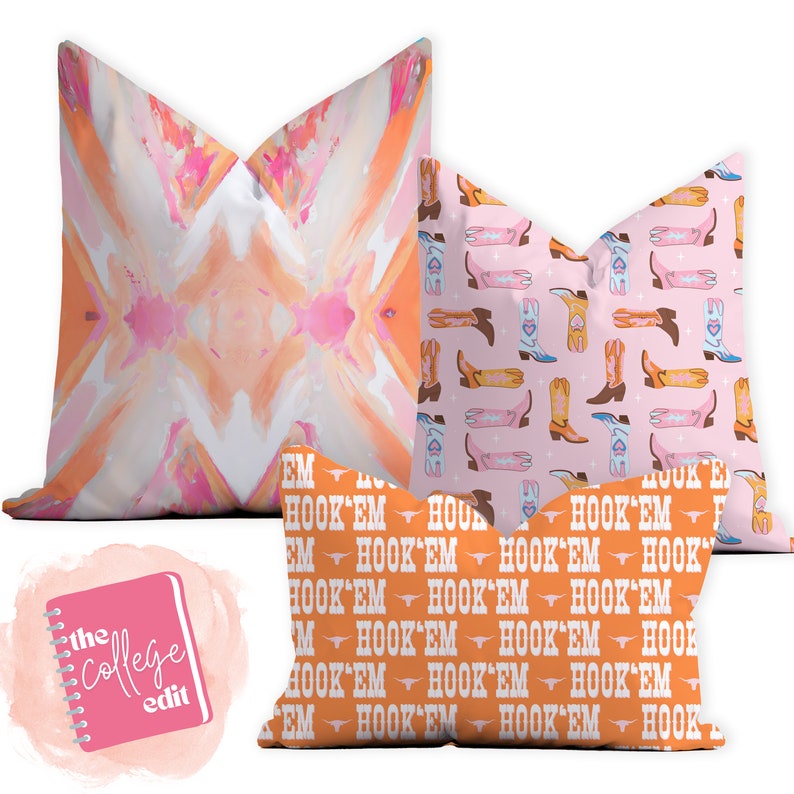 May include: Three decorative throw pillows with different patterns. The first pillow has a pink and orange abstract design. The second pillow has a pink background with a repeating pattern of orange and blue cowboy boots. The third pillow has an orange background with a repeating pattern of white cowboy boots and the text "HOOK'EM" in white.