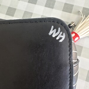 May include: Black and white striped handbag with a white tassel and the initials "WHM" written in white on the side.