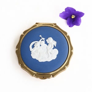May include: A gold compact mirror with a blue enamel background and a white cameo of three cherubs on a cloud.