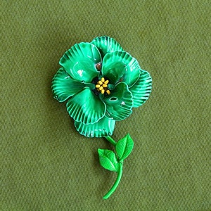 Retro 60s colorful metal flower brooch is bright blue green with round layered petals, yellow pistils, bright green stem with two leaves.