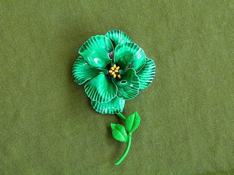 Retro 60s colorful metal flower brooch is bright blue green with round layered petals, yellow pistils, bright green stem with two leaves.