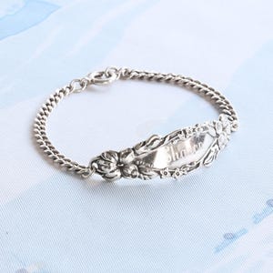 May include: A silver bracelet with a charm that says "Sharon" in a floral design.
