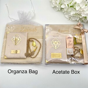 May include: Two gift sets for prayer, one in a clear organza bag and the other in a clear acetate box. Both sets include a prayer rug, a prayer book, a set of prayer beads, and a bookmark. The organza bag set is personalized with the name "Zainab" and the acetate box set is personalized with the name "Ammi Jada".