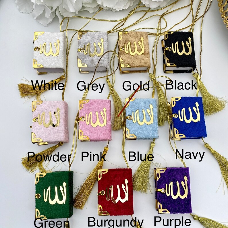 May include: A set of ten small, decorative, velvet-covered books with gold trim and tassels. The books are in various colours, including white, grey, gold, black, powder, pink, blue, navy, green, burgundy, and purple. Each book features a gold Arabic inscription.