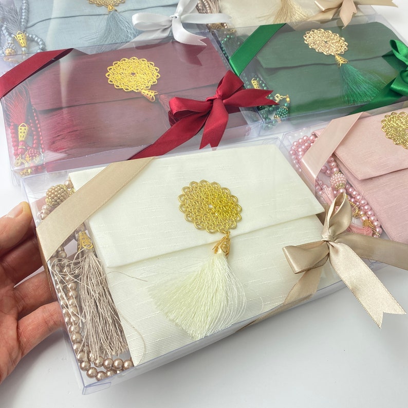 Pu&ograve; includere: Un set di cinque scatole regalo con coperchi in tessuto di diversi colori e dettagli dorati. Ogni scatola contiene una collana di perle da preghiera e un fiocco. Le scatole sono avvolte in plastica trasparente e legate con un nastro.