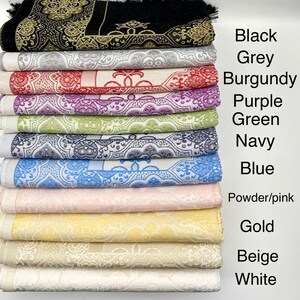 K&ouml;nnte beinhalten: Ein Stapel von 10 Gebetsteppichen in verschiedenen Farben, darunter Schwarz, Grau, Burgunderrot, Lila, Gr&uuml;n, Marineblau, Blau, Puderrosa, Gold, Beige und Wei&szlig;. Die Teppiche sind aus einem weichen, strukturierten Stoff gefertigt und weisen komplizierte Muster auf.