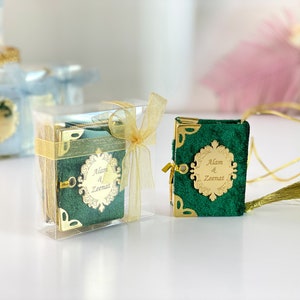 May include: Two small green velvet books with gold trim and a gold inscription that reads "Alam & Zeenat". One book is in a clear plastic box with a gold ribbon. The other book has a gold cord attached to it with a gold tassel.