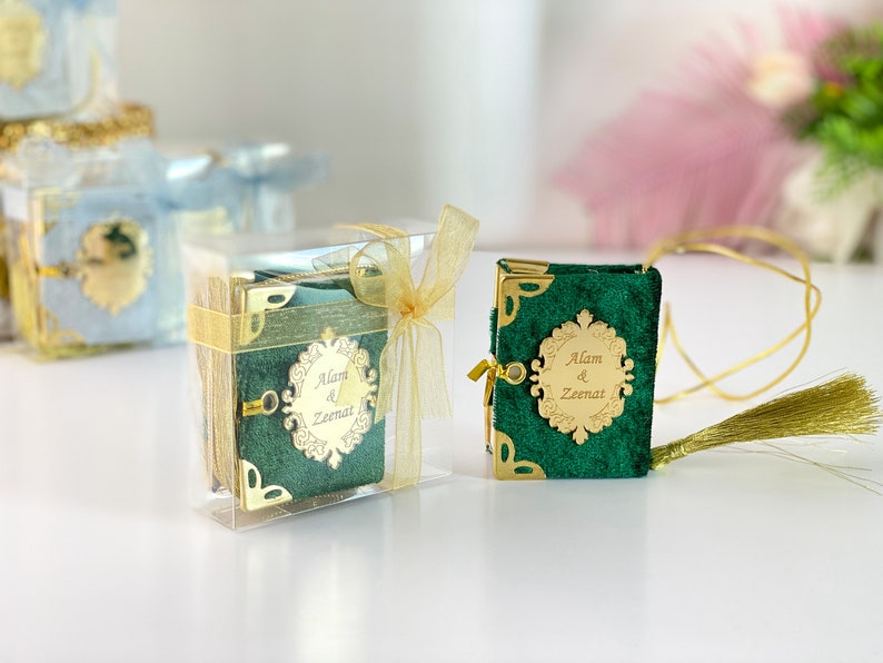 May include: Two small green velvet books with gold trim and a gold inscription that reads "Alam & Zeenat". One book is in a clear plastic box with a gold ribbon. The other book has a gold cord attached to it with a gold tassel.