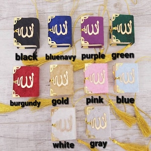 May include: A collection of small, colorful books with gold accents and tassels. The books are in various colors, including black, blue, purple, green, burgundy, gold, pink, blue, white, and gray. Each book features gold lettering.