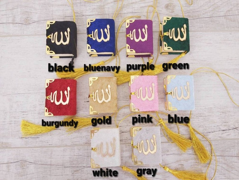 May include: A collection of small, colorful books with gold accents and tassels. The books are in various colors, including black, blue, purple, green, burgundy, gold, pink, blue, white, and gray. Each book features gold lettering.