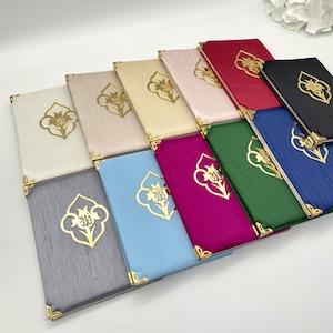 May include: A collection of 11 different colored prayer books with gold accents and a decorative design. The books are arranged in a row, with the darkest color at the back and the lightest color at the front.