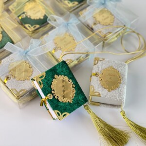 May include: Two small, decorative books with gold trim and tassels. One book is green velvet with a gold inscription that reads "Alan & Zarina". The other book is white velvet with a gold inscription that reads "Alan & Zarina".