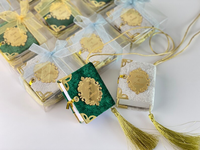 May include: Two small, decorative books with gold trim and tassels. One book is green velvet with a gold inscription that reads "Alan & Zarina". The other book is white velvet with a gold inscription that reads "Alan & Zarina".