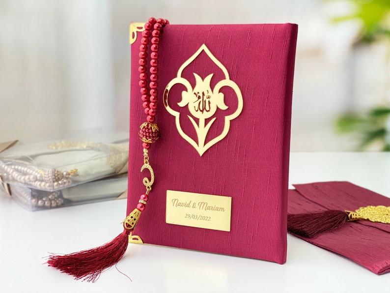 Pu&ograve; includere: Un libro di preghiere color borgogna con un fiocco dorato e un'iscrizione dorata che recita "Navid & Mariam 29/03/2022". Il libro ha un design decorativo dorato sulla copertina.
