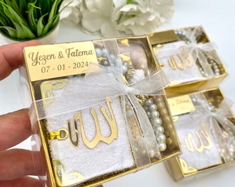 May include: Gold gift boxes with white fabric and a gold Allah calligraphy design. Each box includes a white pearl necklace and a small gold charm. The box has a personalized label with the names "Yezen & Fatema" and the date "07-01-2024".