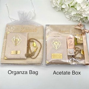 May include: Two gift sets for prayer, one in a clear organza bag and the other in a clear acetate box. Both sets include a prayer rug, a prayer book, a set of prayer beads, and a bookmark. The organza bag set is personalized with the name "Zainab" and the acetate box set is personalized with the name "Ammi Jada".