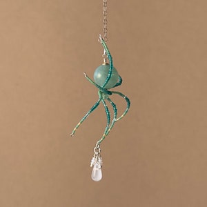 May include: A beaded spider charm with a teal green gemstone and a clear crystal drop pendant.