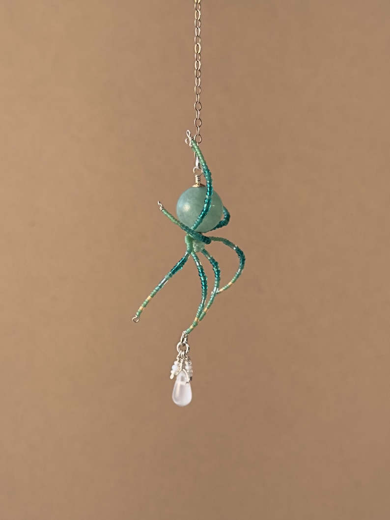 May include: A beaded spider charm with a teal green gemstone and a clear crystal drop pendant.