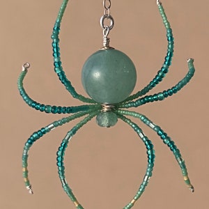 May include: A teal blue beaded spider with a green stone body hanging from a silver chain.