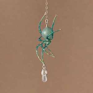 May include: A beaded spider pendant with a green and blue iridescent body and a clear teardrop crystal hanging from it.