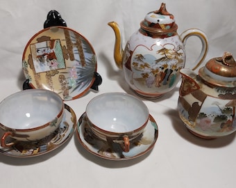 May include: A vintage Japanese tea set with a teapot, two teacups, and saucers. The set features intricate hand-painted floral and landscape designs in shades of gold, red, and blue.