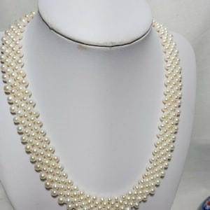 Op de afbeelding: Een witte parelketting met meerdere strengen parels. De ketting ligt op een witte mannequinbuste.