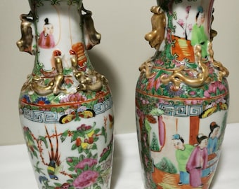 May include: Two antique Chinese porcelain vases with intricate floral and figural designs. The vases are decorated with gold accents and feature a vibrant color palette.