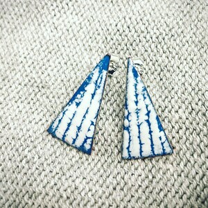 May include: A pair of blue and white triangle shaped earrings. The earrings have a white background with blue lines and are made of metal.