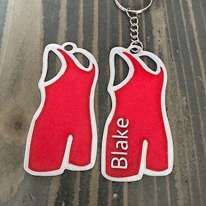 May include: Red wrestling singlet keychain with a white outline and the name "Blake" printed on the front.