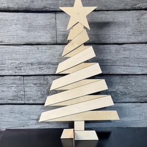 May include: A wooden Christmas tree decoration with a star on top. The tree is made of multiple layers of wood that are stacked on top of each other. The tree is standing on a wooden base.
