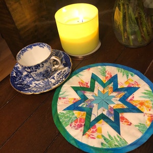 Puede incluir: Una taza de té y un platillo de porcelana azul y blanco con un patrón floral. La taza de té y el platillo están sobre una mesa de madera junto a un posavasos de tela azul verdoso y verde con un diseño de estrella.