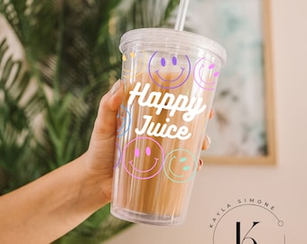 May include: A clear plastic tumbler with a straw, featuring a colorful smiley face design and the text "Happy Juice". The tumbler is held by a hand in front of a blurred background.