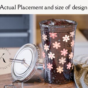 May include: A clear tumbler with a black lid and a straw. The tumbler is decorated with pink and peach flowers. The tumbler is filled with a dark liquid and ice.