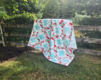 Puede incluir: Una colcha blanca con un diseño de patchwork con estrellas rojas, verdes y blancas. La colcha está colgada en un tendedero delante de una valla de madera.