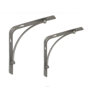 Puede incluir: Dos escuadras de estantería de metal gris. Cada escuadra tiene una parte superior plana con un agujero para el montaje, un soporte curvo y una base vertical con un agujero. Las escuadras están diseñadas para soportar estantes.
