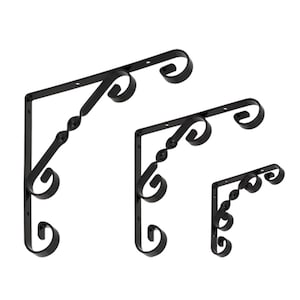 Può includere: Tre staffe per mensole in metallo nero con decorazioni a volute. Le staffe sono di dimensioni diverse, la più grande in alto e la più piccola in basso.
