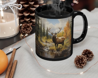 May include: Black coffee mug with a scenic image of an elk standing in a forest stream. The mug has a white rim and handle.