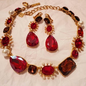 May include: A gold-toned necklace and matching earrings set. The necklace features large, faceted red and brown gemstones, interspersed with faux pearls. The earrings have a similar design, with a large teardrop-shaped red gemstone.
